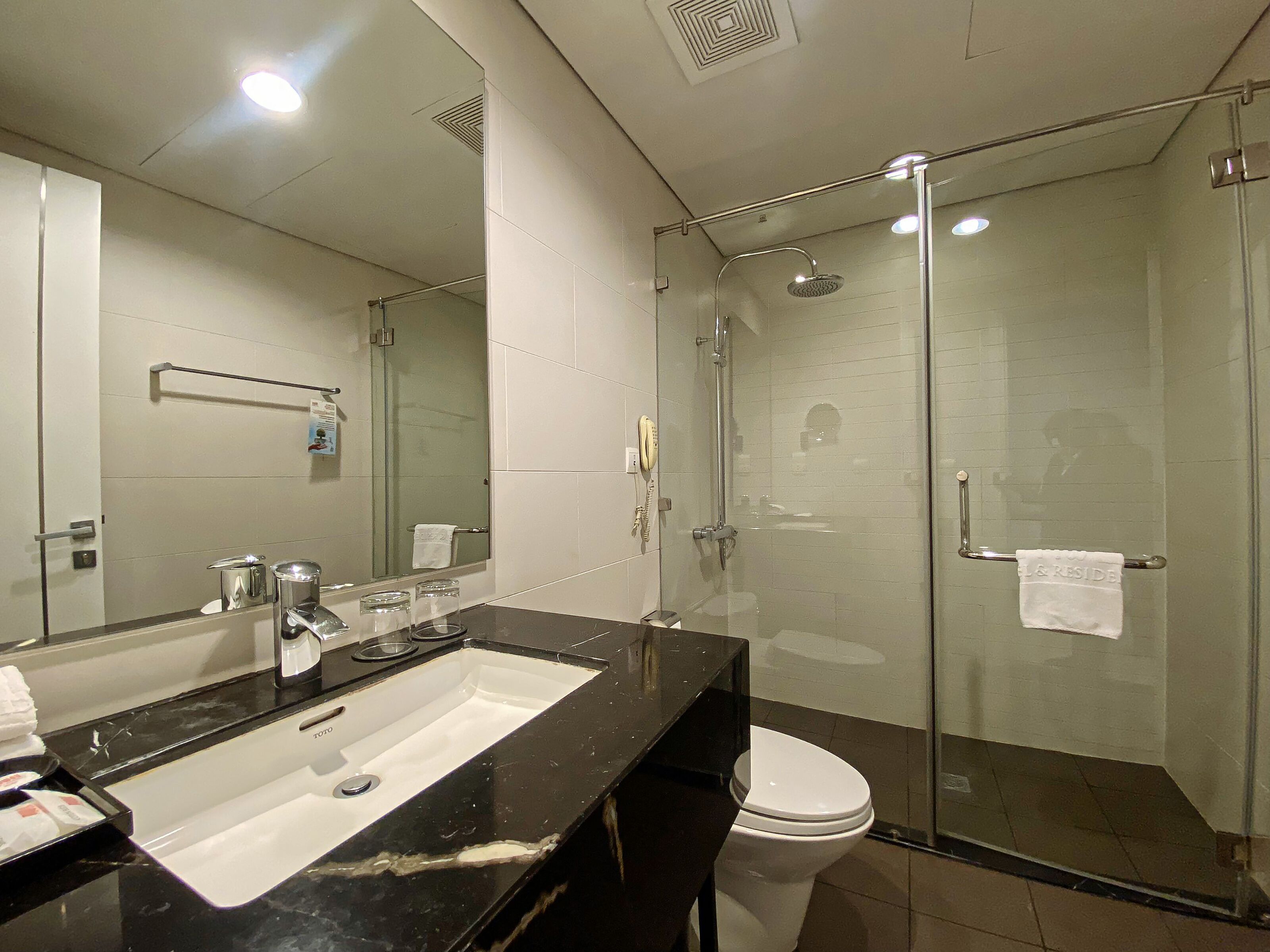 Une salle de bain moderne avec une douche à parois de verre, un grand miroir et un lavabo sur un plan de toilette noir.