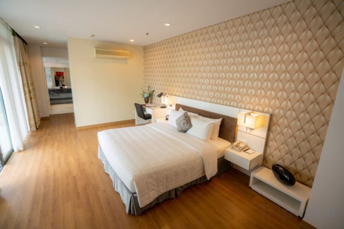 A hotel room with a large bed, bedside tables, a desk, and a view of the hallway.