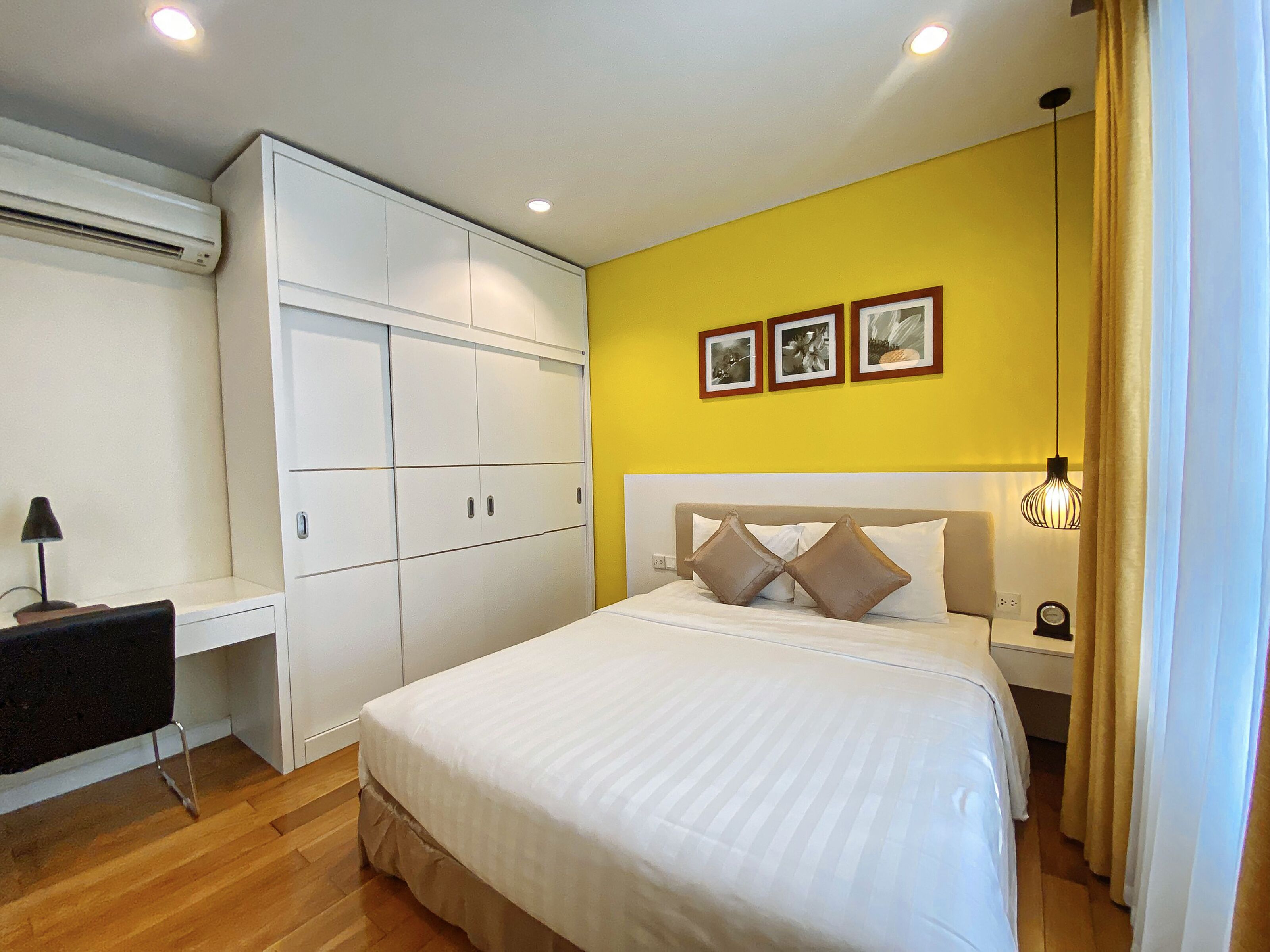 Une chambre à coucher comprenant un lit, un bureau, une armoire et un mur orné de trois tableaux encadrés.