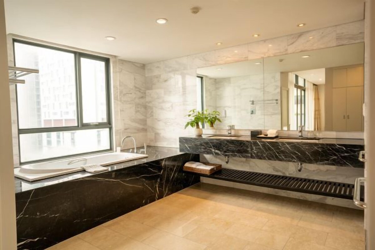A modern bathroom with a large window, a black marble vanity, a white sink, and a mirror.