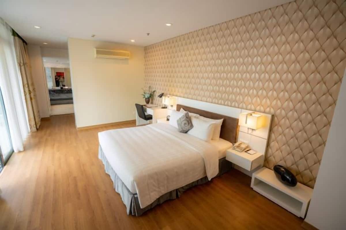 A hotel room with a large bed, a bedside table with a lamp, a headboard with a quilted pattern, and a view of a staircase.