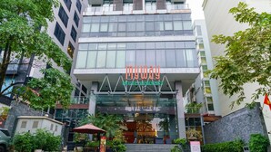 Una entrada de hotel moderna con fachada de vidrio, asientos al aire libre y plantas en macetas.