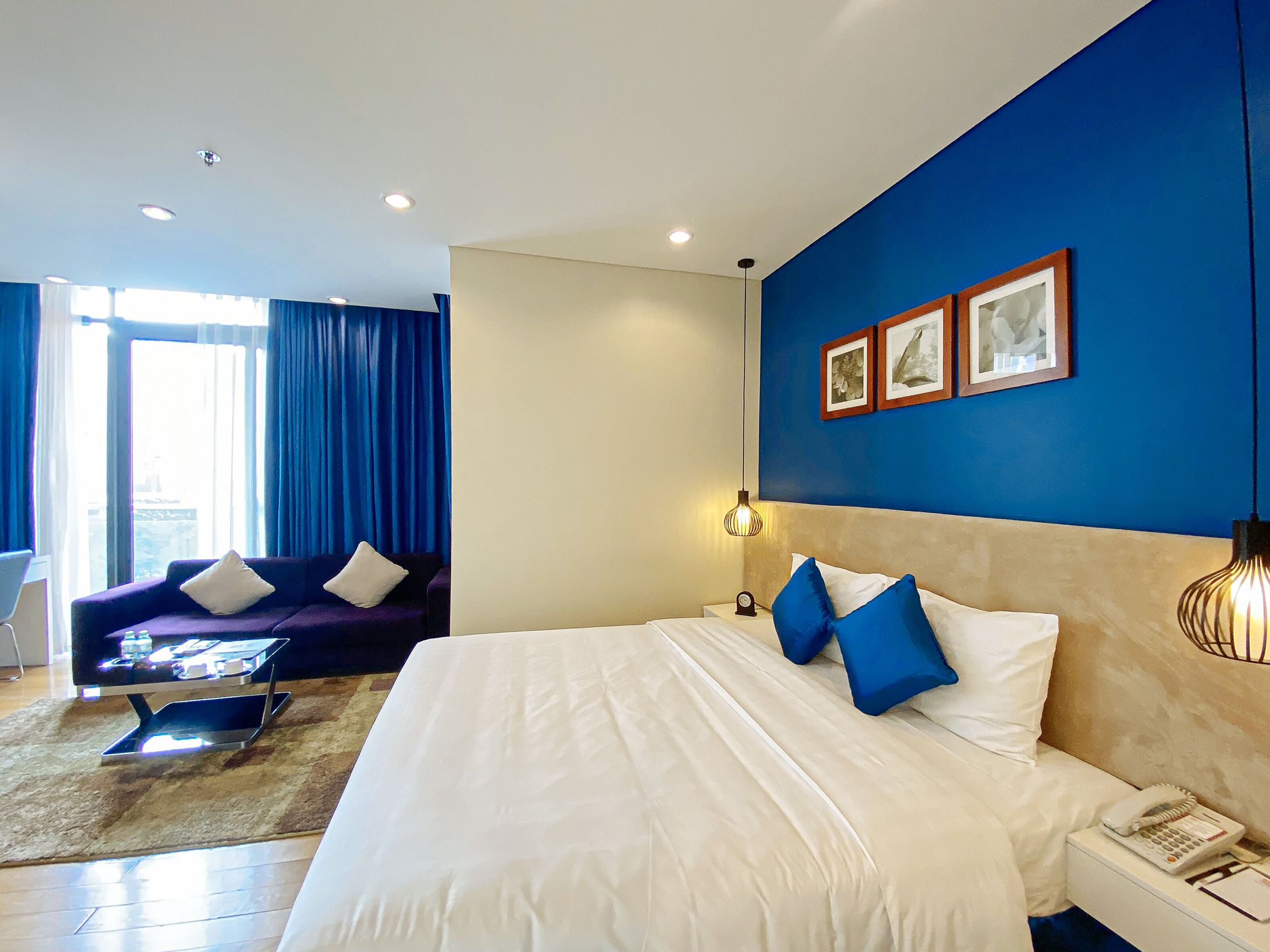 A hotel room with a large bed, a sofa, a desk with a lamp, and a window with curtains.