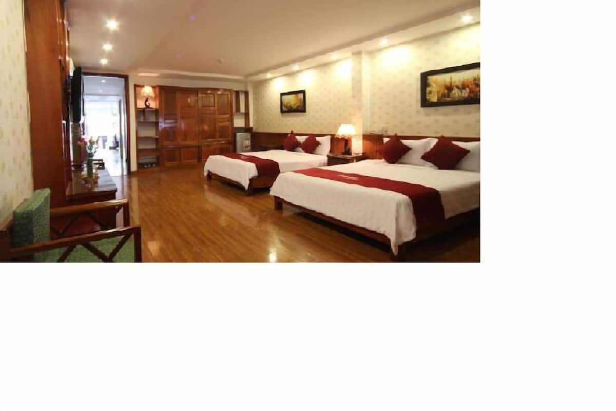 A hotel room with two beds, a wooden floor, a desk with a chair, and a door leading to a bathroom.