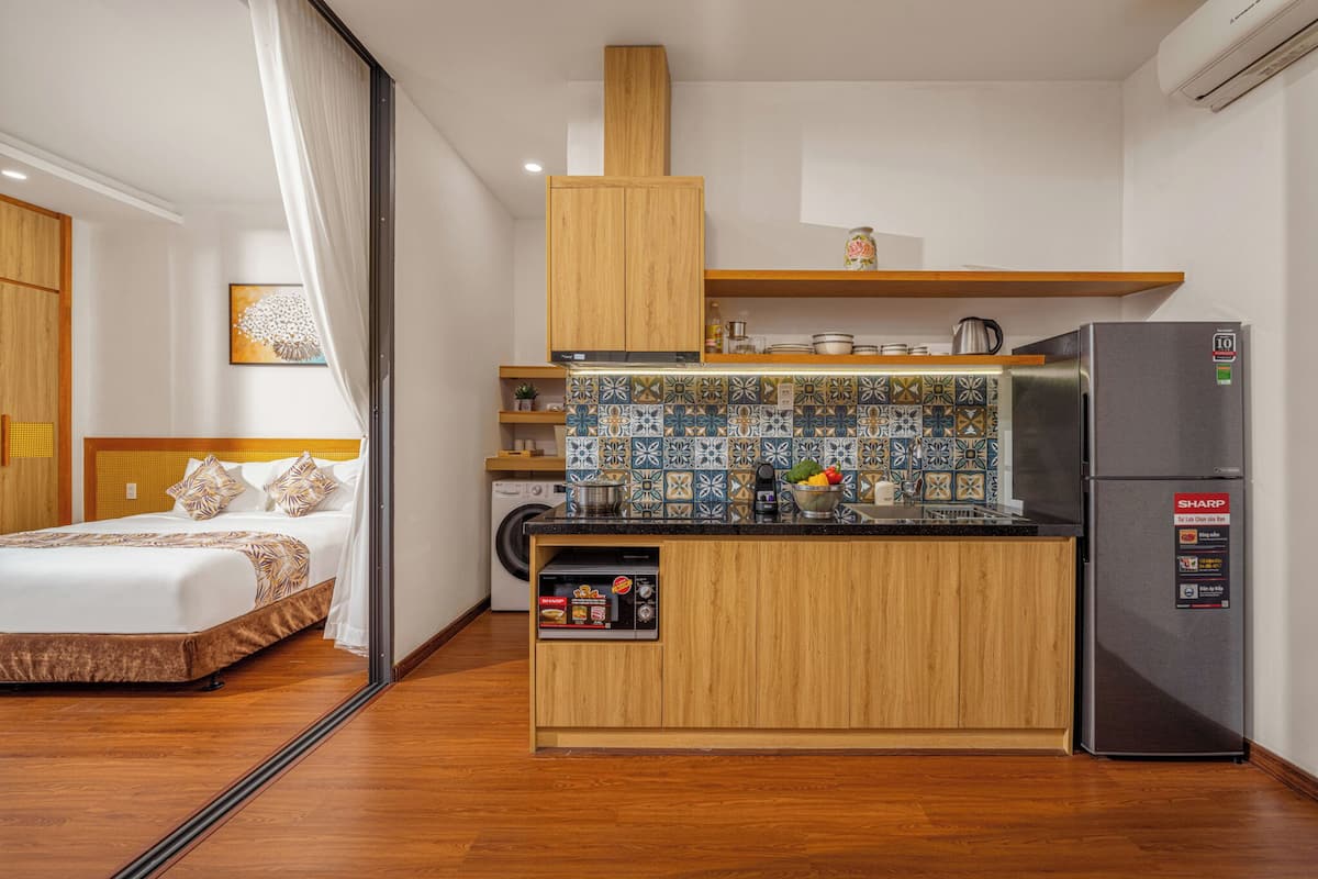 A compact hotel room with a kitchenette, a bed, and a washing machine.