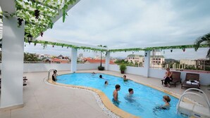 En udendørs swimmingpool med folk, der svømmer og slapper af.