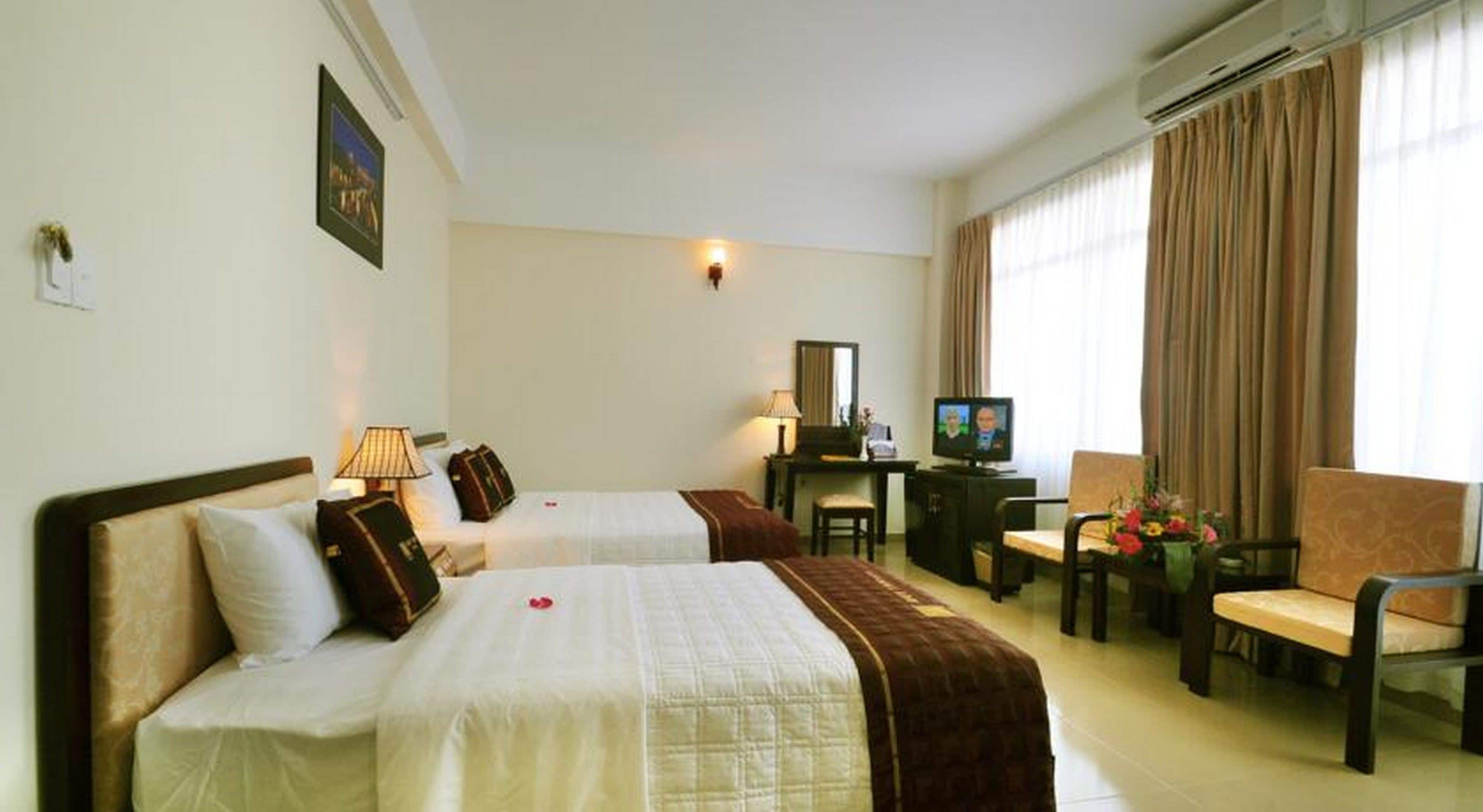 A hotel room with two beds, a desk, a chair, a television, and a window with curtains.