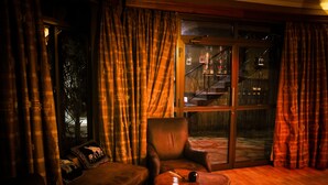 A dimly lit room with a leather armchair, a small round table, and a large window with curtains. - Zawadi House (Arusha)