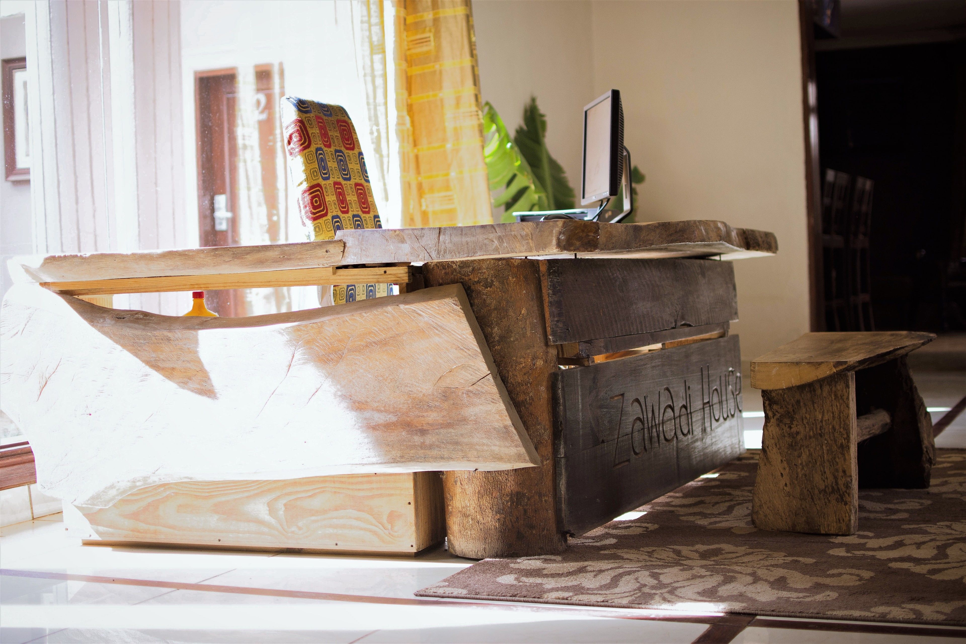 A reception desk with a wooden design, a computer monitor, and a sign that reads "Zawadi House".