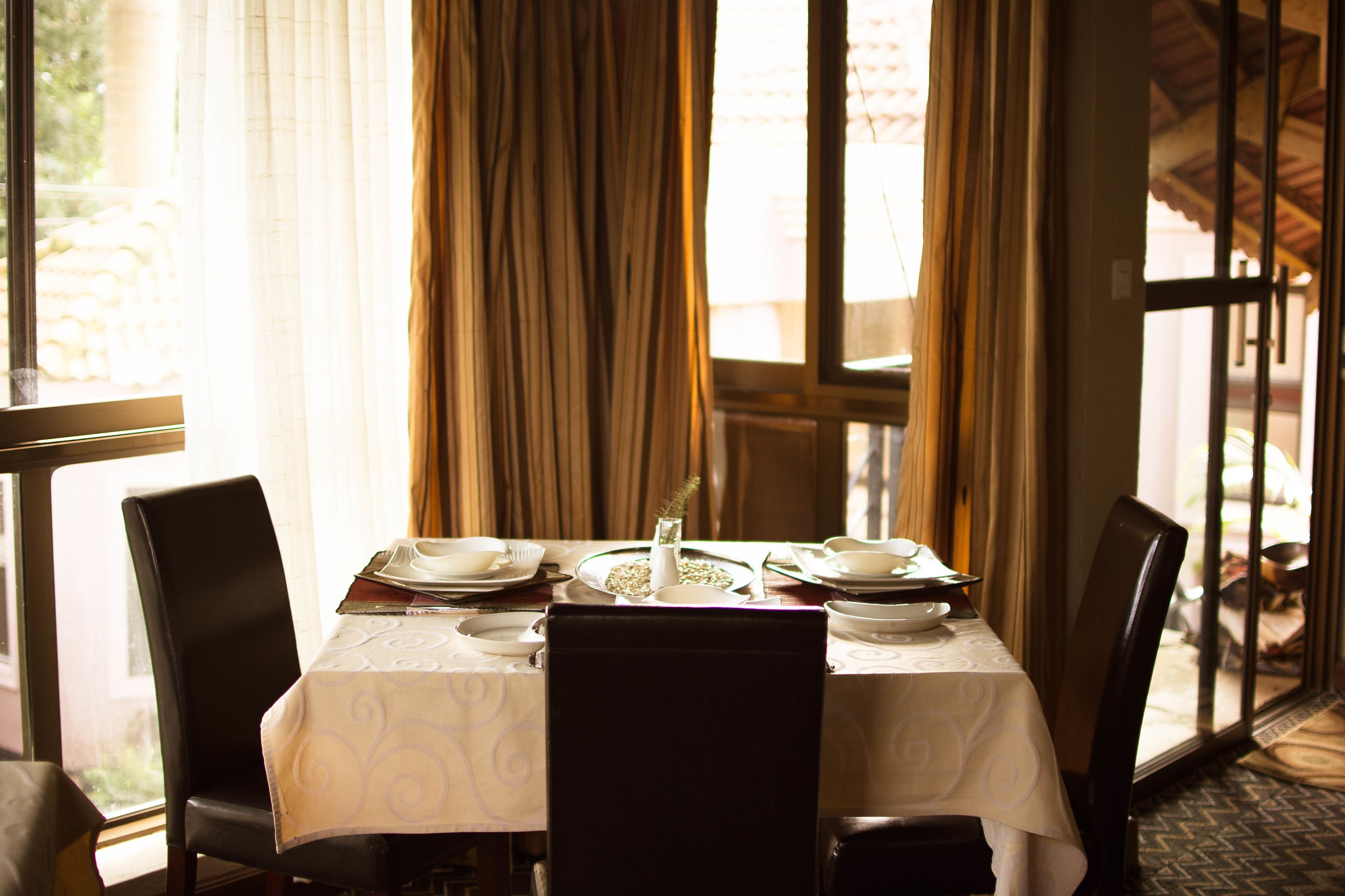 Une table à manger dressée pour quatre personnes, avec des chaises, un vase et une fenêtre avec des rideaux.