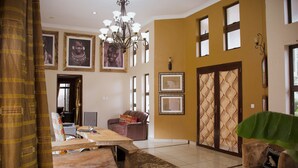 A spacious living area with a large wooden table, a sofa, and a patterned rug. There are framed pictures on the walls and a chandelier hanging from the ceiling. - Zawadi House (Arusha)