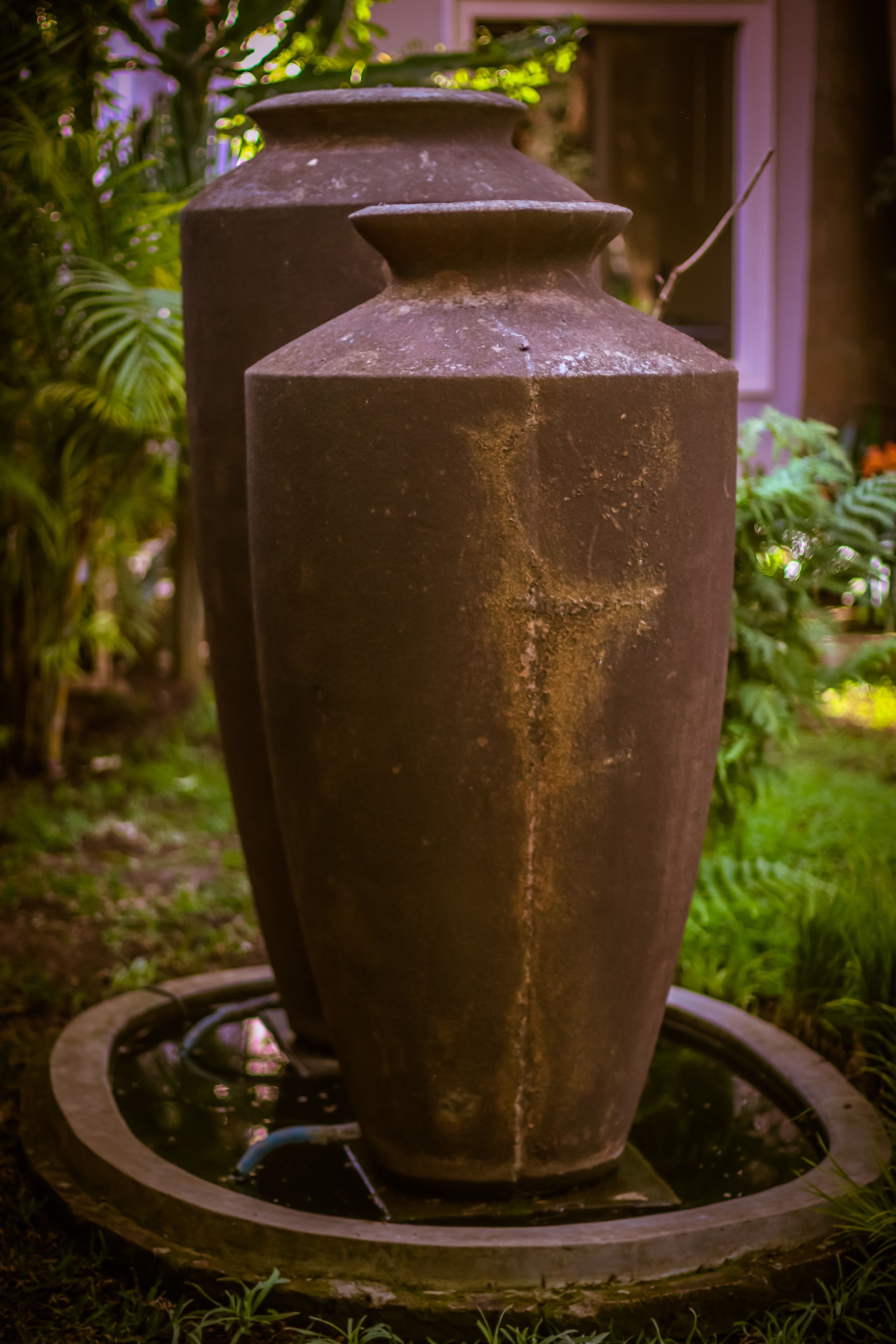 Two large vases on a circular platform in a garden setting.
