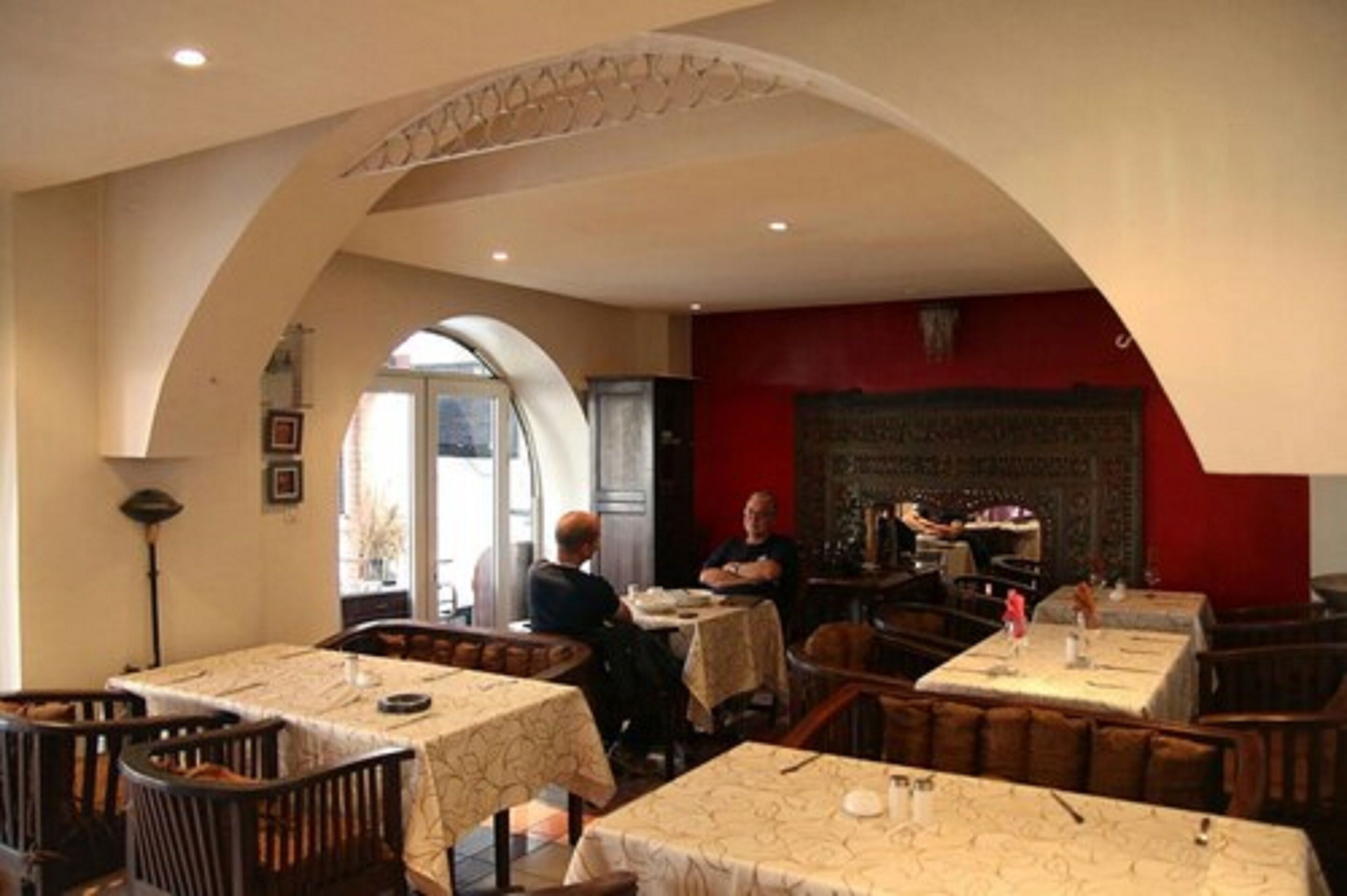 A restaurant with high arched ceilings, multiple tables with white tablecloths, and a red accent wall.