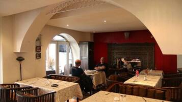 A restaurant with high arched ceilings, multiple tables with white tablecloths, and a red accent wall.
