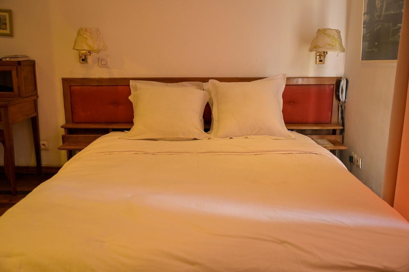 A neatly made bed with white linens, a wooden headboard, and two bedside lamps.