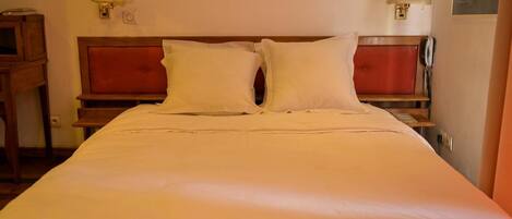 A neatly made bed with white linens, a wooden headboard, and two bedside lamps.