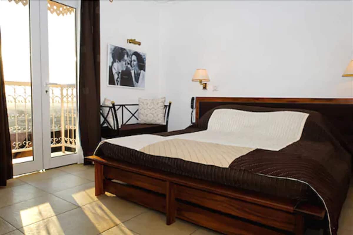 A bedroom with a bed, a chair, a nightstand, a lamp, and a picture on the wall.