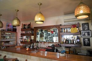 Un bar con lámparas colgantes, estantes con botellas y un espejo que refleja el salón.