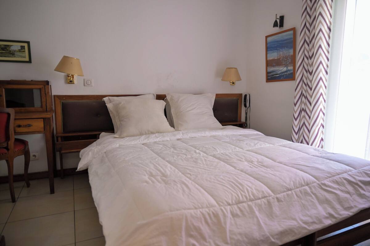 A hotel room with a large bed, two bedside lamps, a desk with a chair, and a painting on the wall.