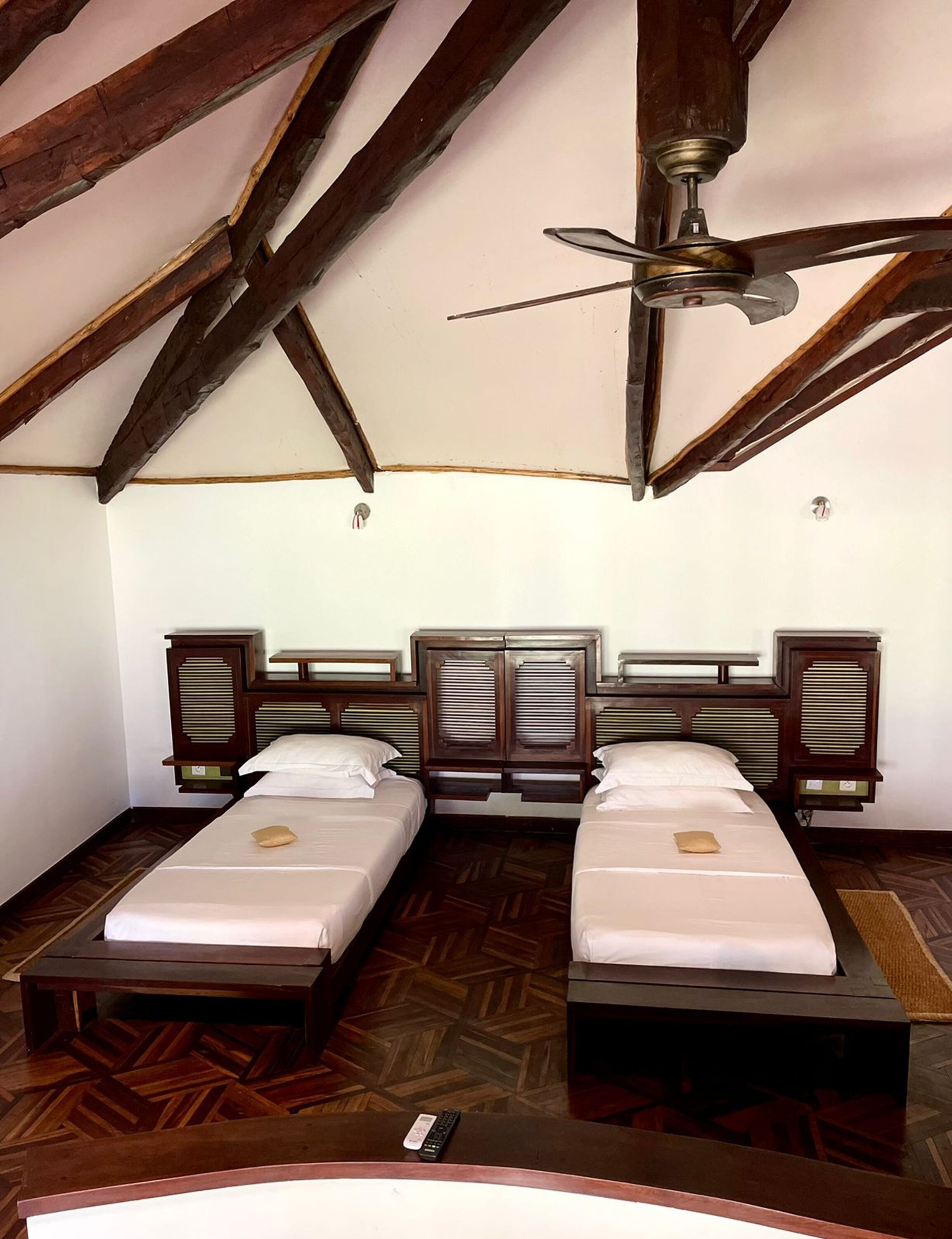 A room with two beds, wooden headboards, a ceiling fan, and a wooden floor.