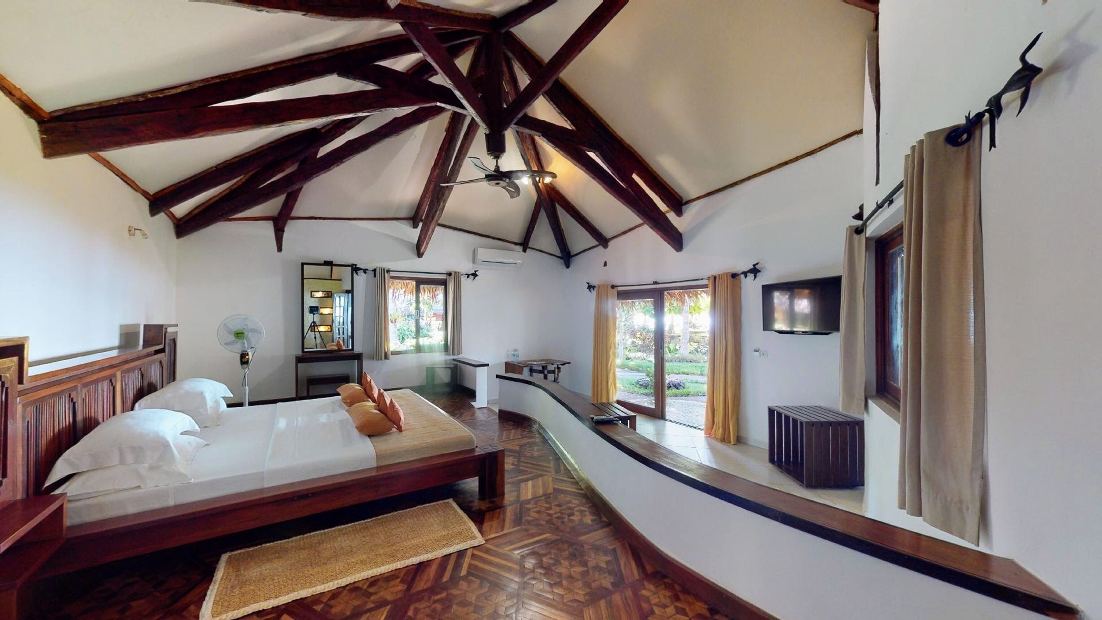 Una habitación amplia con una cama grande, un escritorio, un espejo y un televisor.