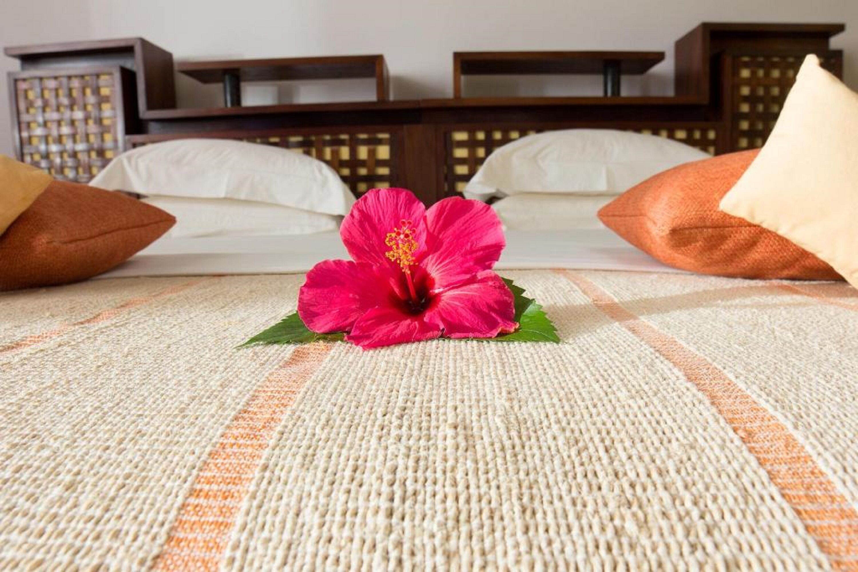 A hotel room with a bed, pillows, and a hibiscus flower on the bedspread.