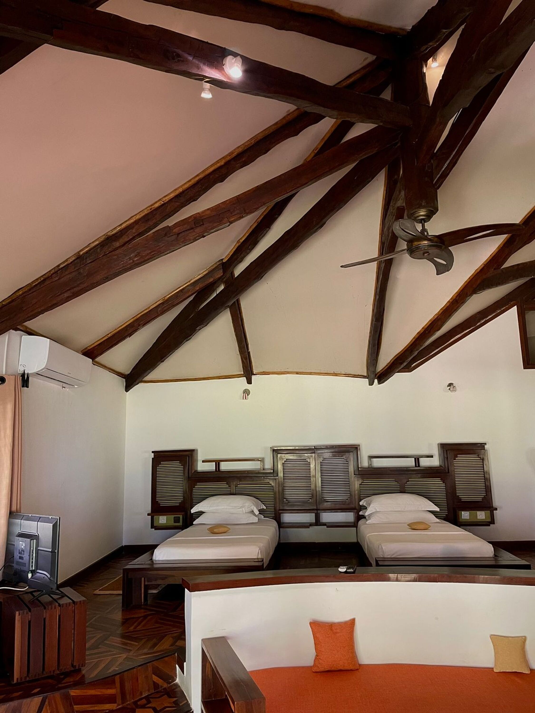 A room with two beds, a ceiling fan, and a wooden ceiling structure.