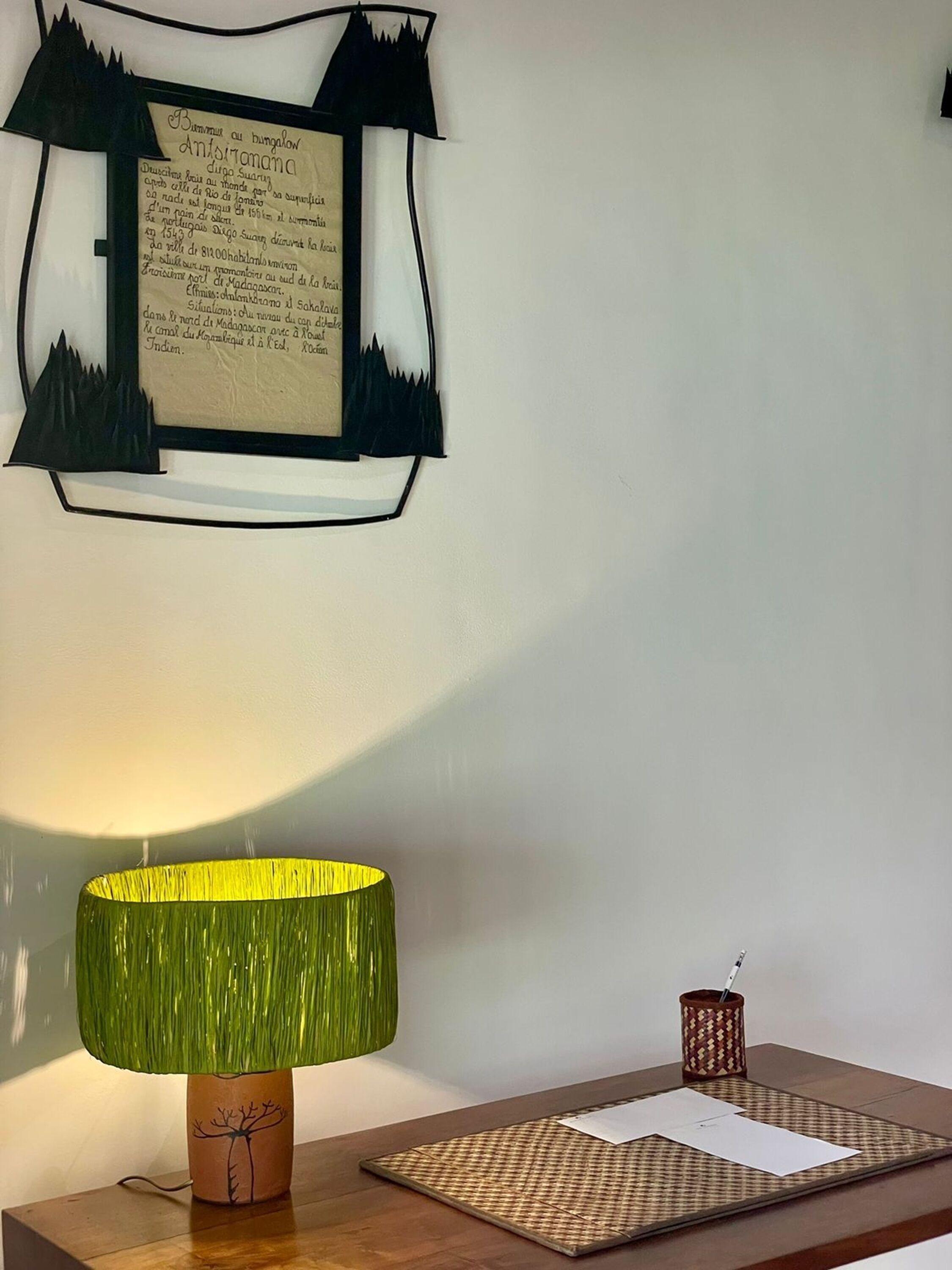 Una habitación con una lámpara sobre una mesa de madera, un documento enmarcado en la pared y un pequeño adorno en la mesa.