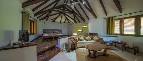A spacious living area with a high ceiling, wooden beams, a sofa set, a coffee table, and a television.