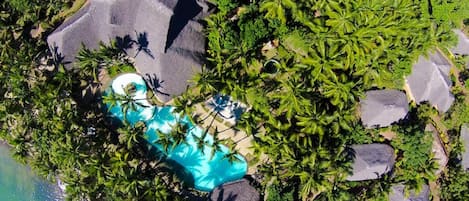Vue aérienne d’un complexe hôtelier doté d’une piscine entourée de palmiers et de gros rochers.