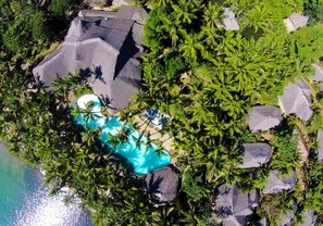 Vue aérienne d’un complexe hôtelier doté d’une piscine entourée de palmiers et de gros rochers.