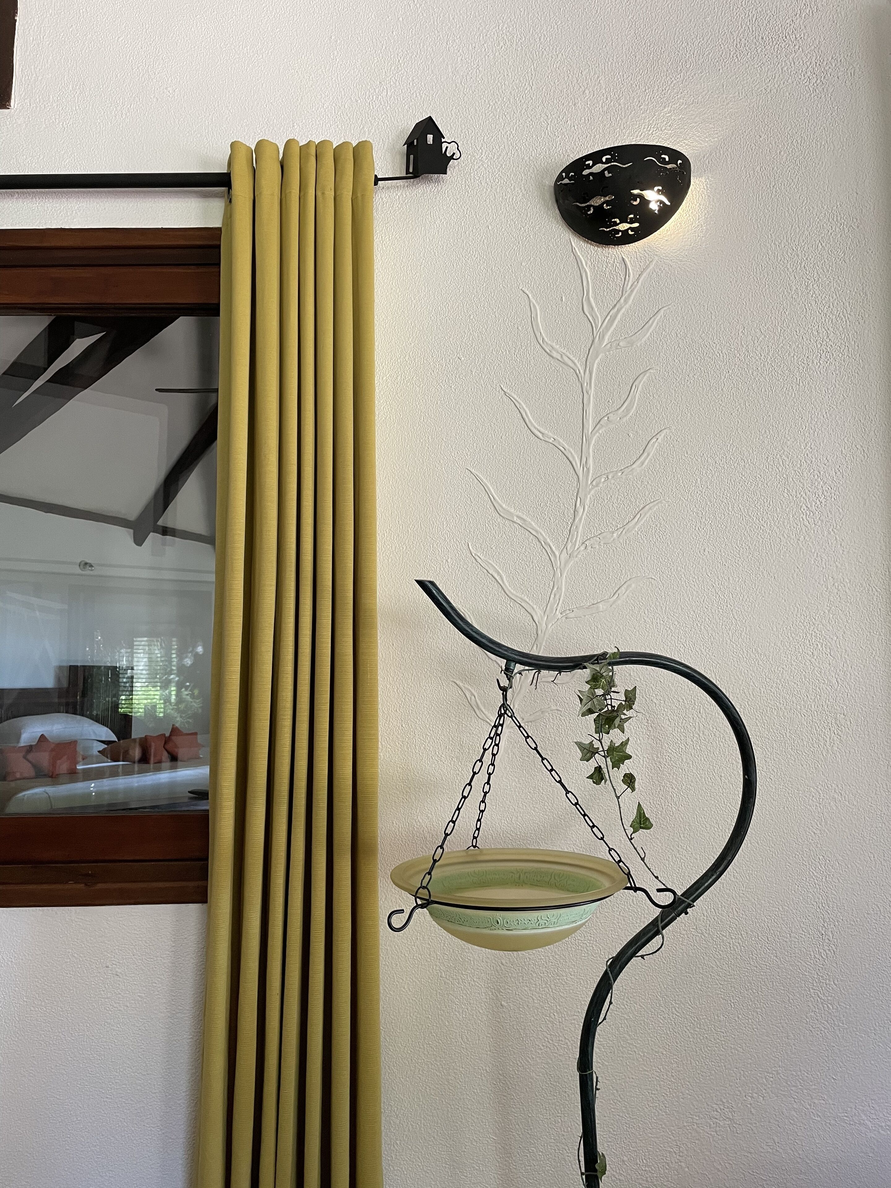 A room with a window, a radiator, a wall-mounted scale with a plant, and a wall decoration.