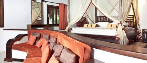 A bedroom with a bed under a mosquito net, a wooden sofa with cushions, and a large mirror on the wall.