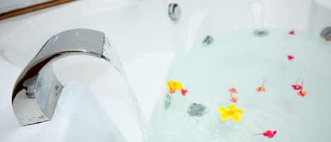 A bathtub with a running faucet and floral decorations in the water.