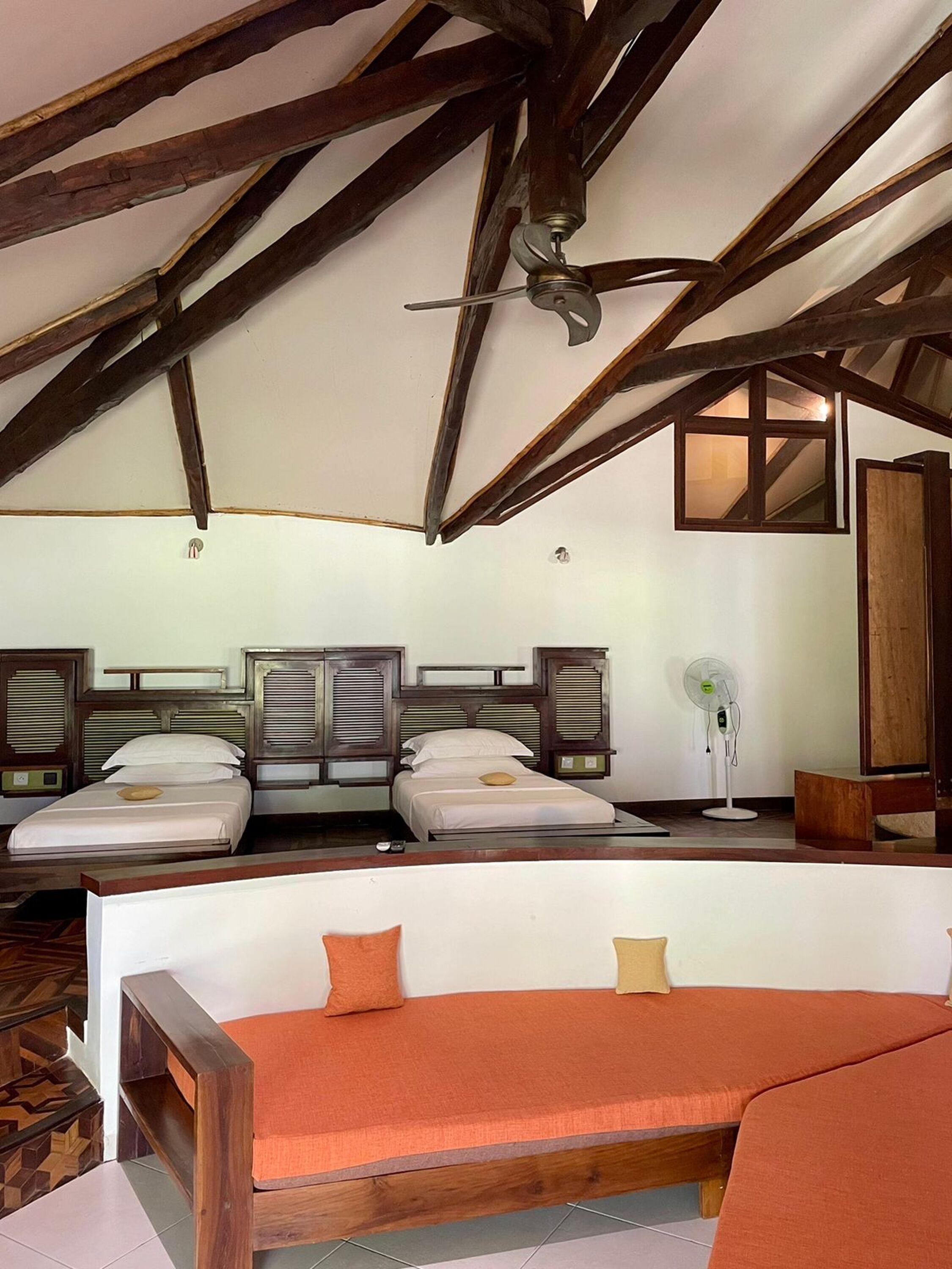 A room with two beds, wooden beams, a ceiling fan, and a window.