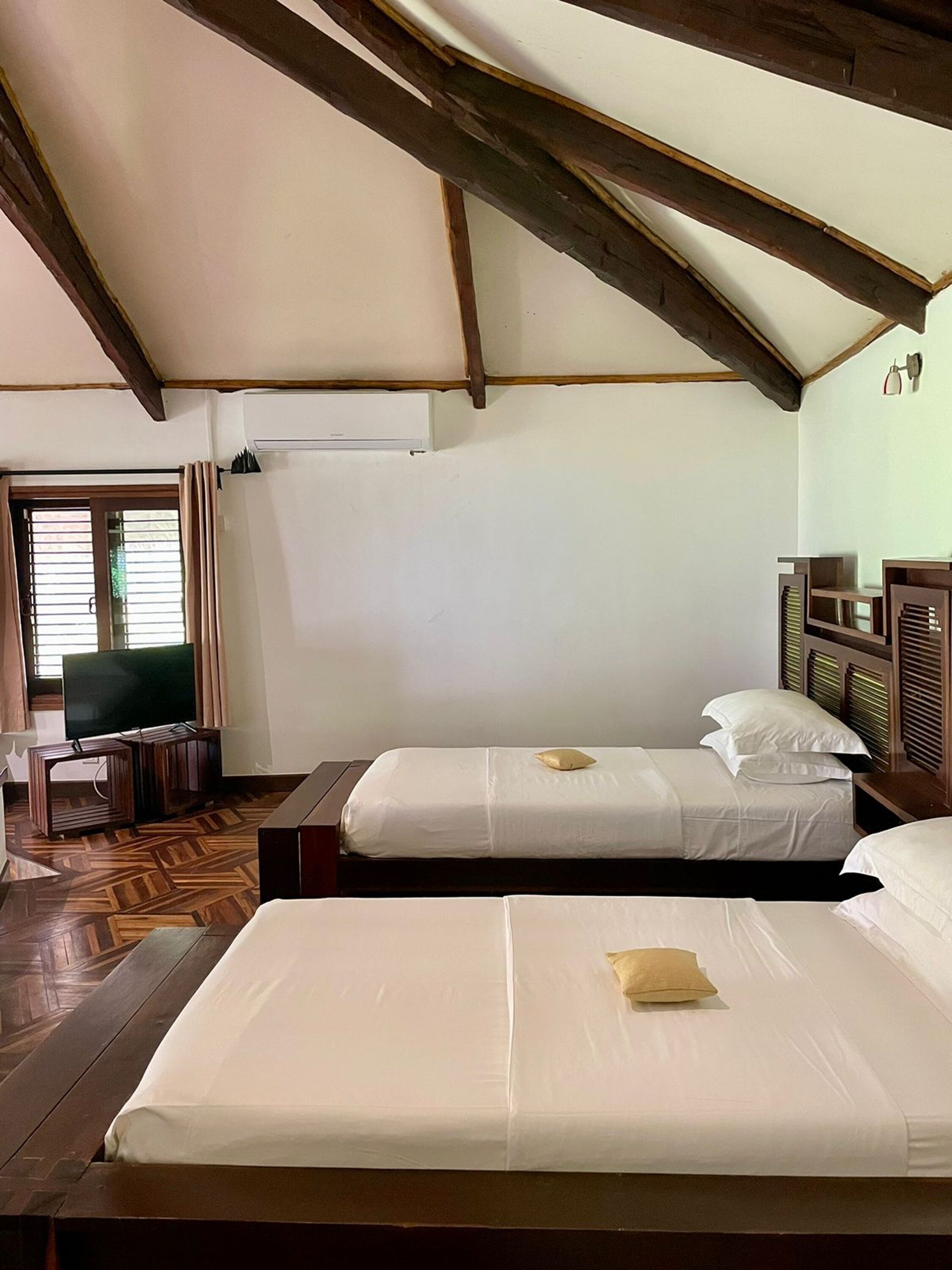 A room with two beds, a television, and a wooden floor.