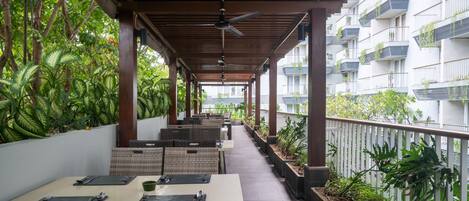 A covered outdoor dining area with wicker furniture and potted plants.