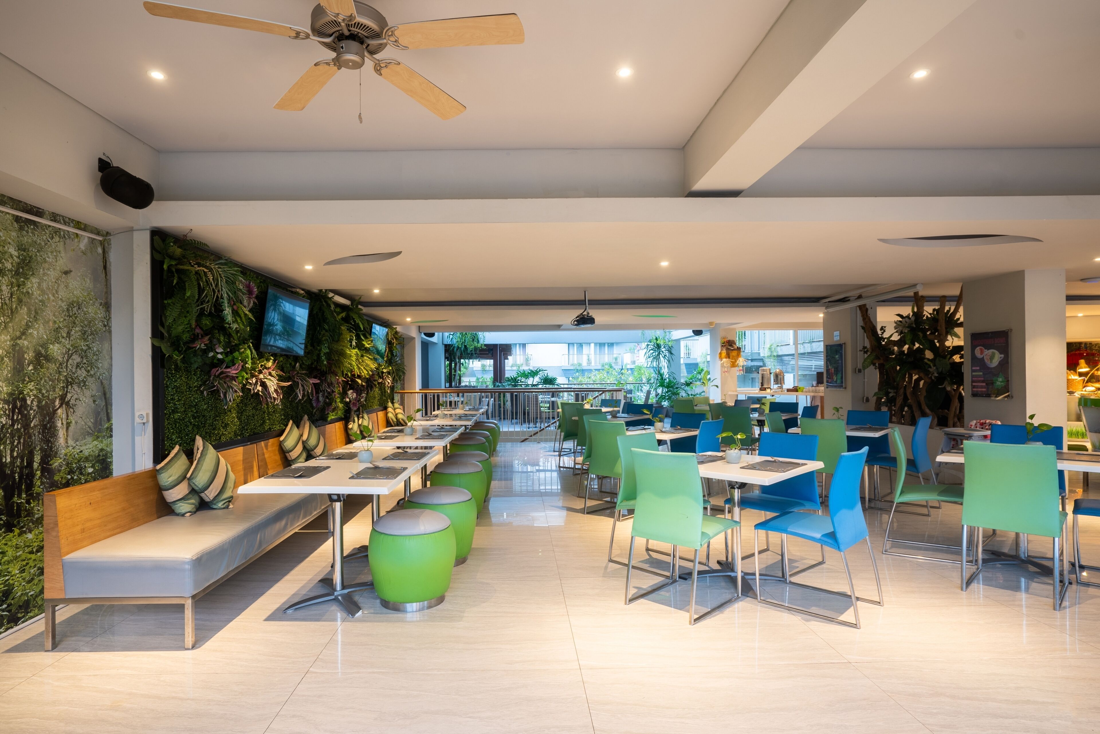 A modern cafe with green and blue seating, a flat-screen TV, and a ceiling fan.