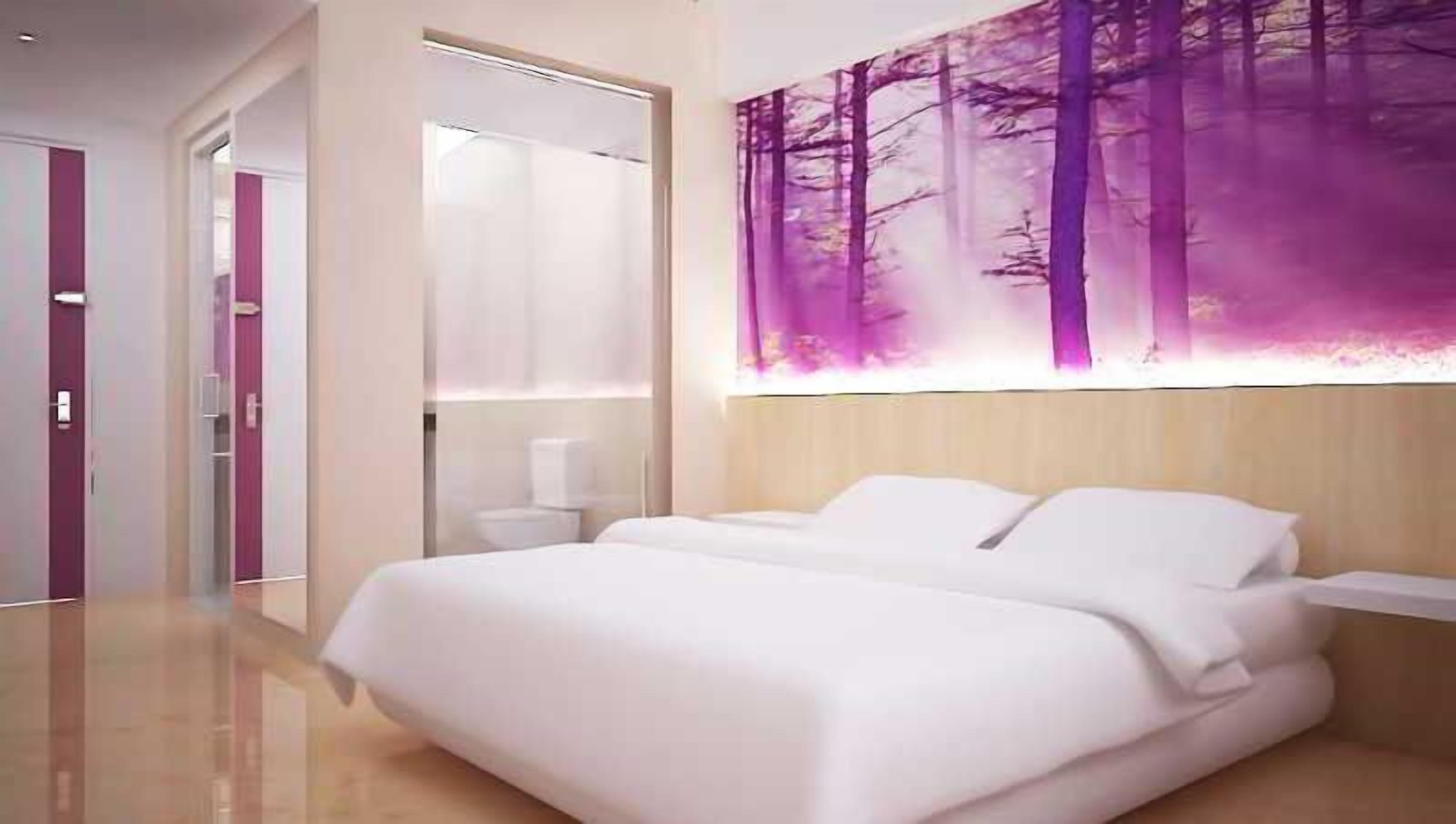 Una habitación de hotel moderna con una cama grande, un baño con espejo y una obra de arte colgada en la pared.