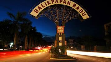 Vista nocturna de una calle con un gran cartel que dice 'BALIKPAPAN BARU' y una torre del reloj.