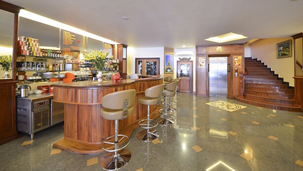 A bar area with stools, a kitchen in the background, and a staircase leading to an elevator. - Golden House International Hotel (Phnom Penh)