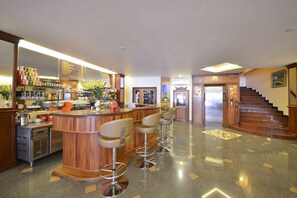 A bar area with stools, a kitchen in the background, and a staircase leading to an elevator. - Golden House International Hotel (Phnom Penh)