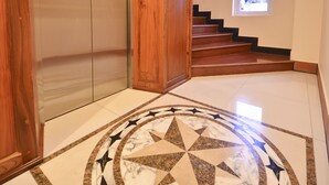 An elevator with a wooden panel design, a marble floor with a star pattern, and a staircase with a window at the top. - Golden House International Hotel (Phnom Penh)