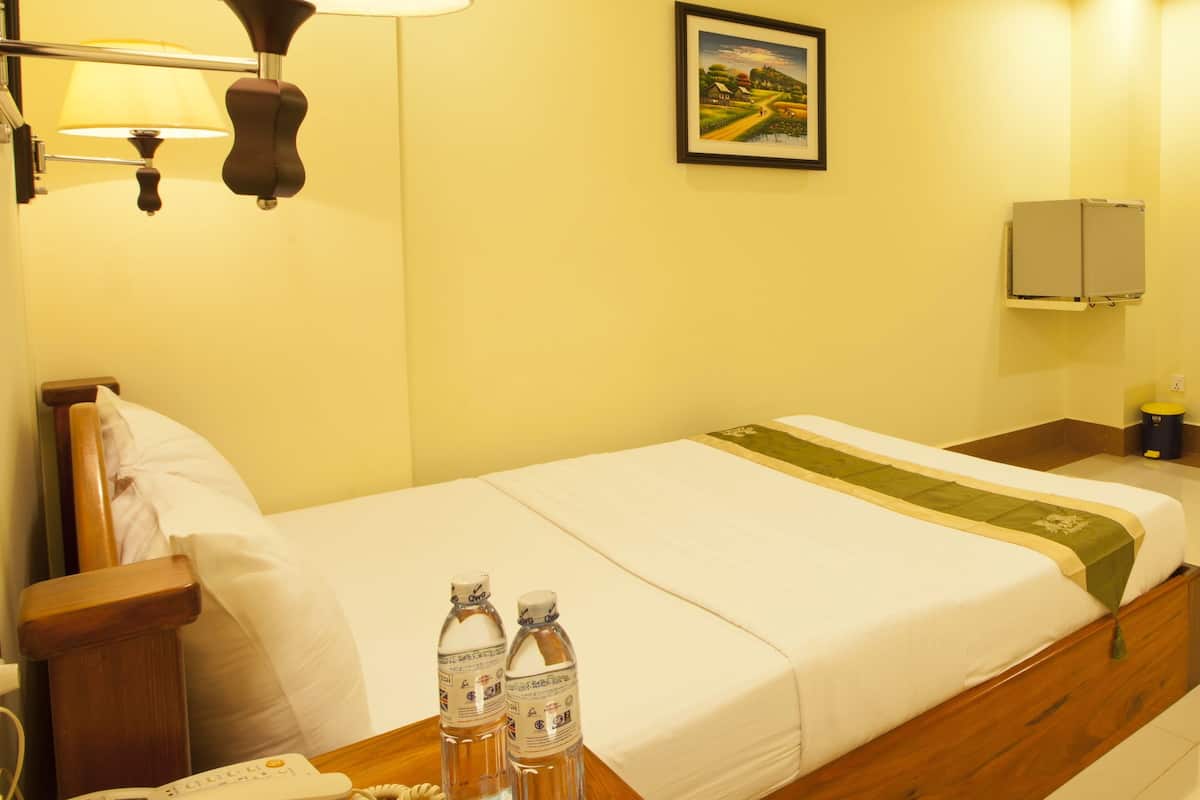 Ein Hotelzimmer mit Bett, Nachttisch, Lampe, Fernseher und einer Vase mit Blumen.