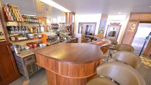 A bar area with a wooden bar counter, seating, and various bottles and glasses on shelves. - Golden House International Hotel (Phnom Penh)