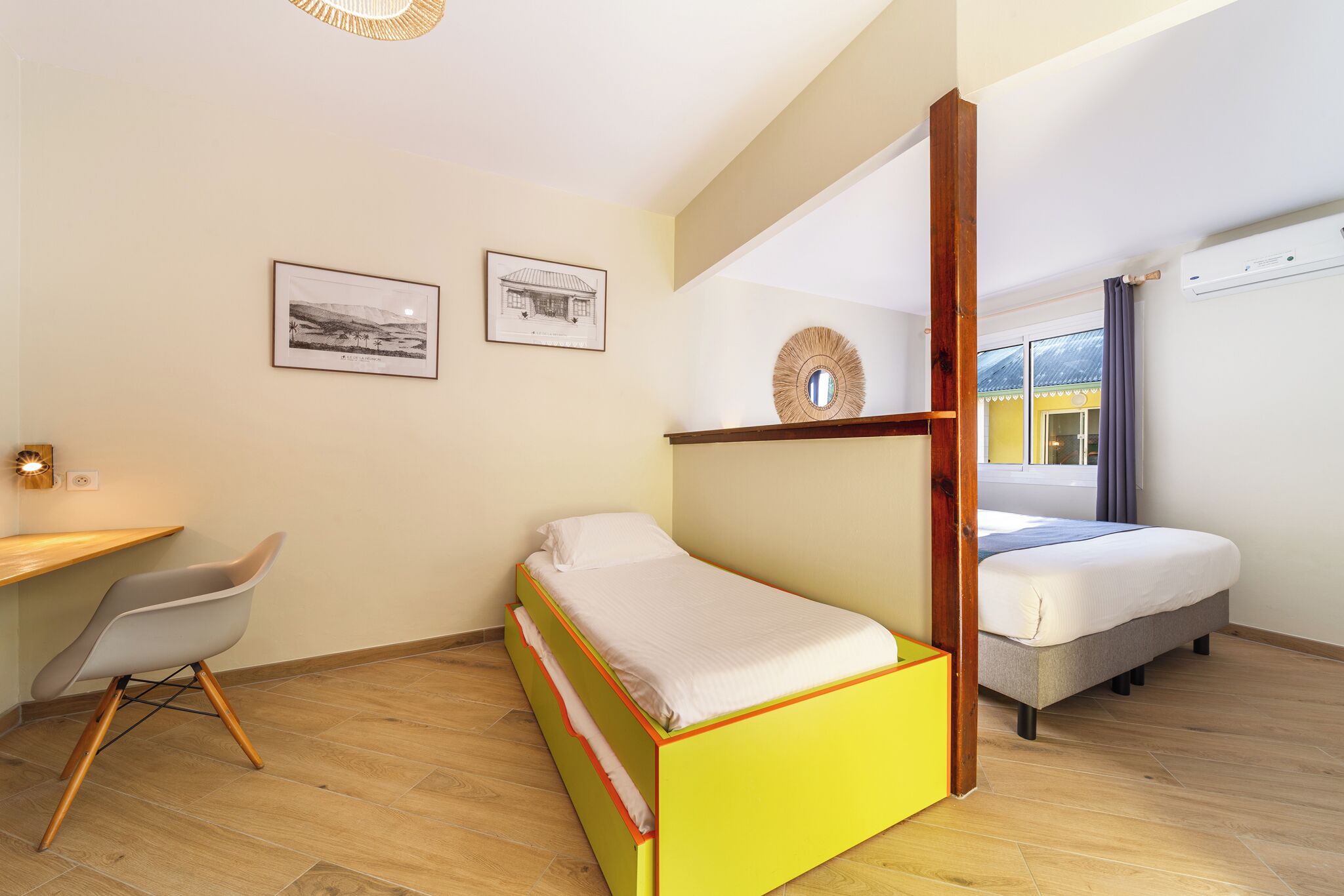 Een compacte kamer met een bed, een bureau en een stoel. Twee ingelijste foto’s hangen aan de muur.