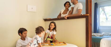 A family in a hotel room with a bunk bed, a children's play area, and a window with curtains.