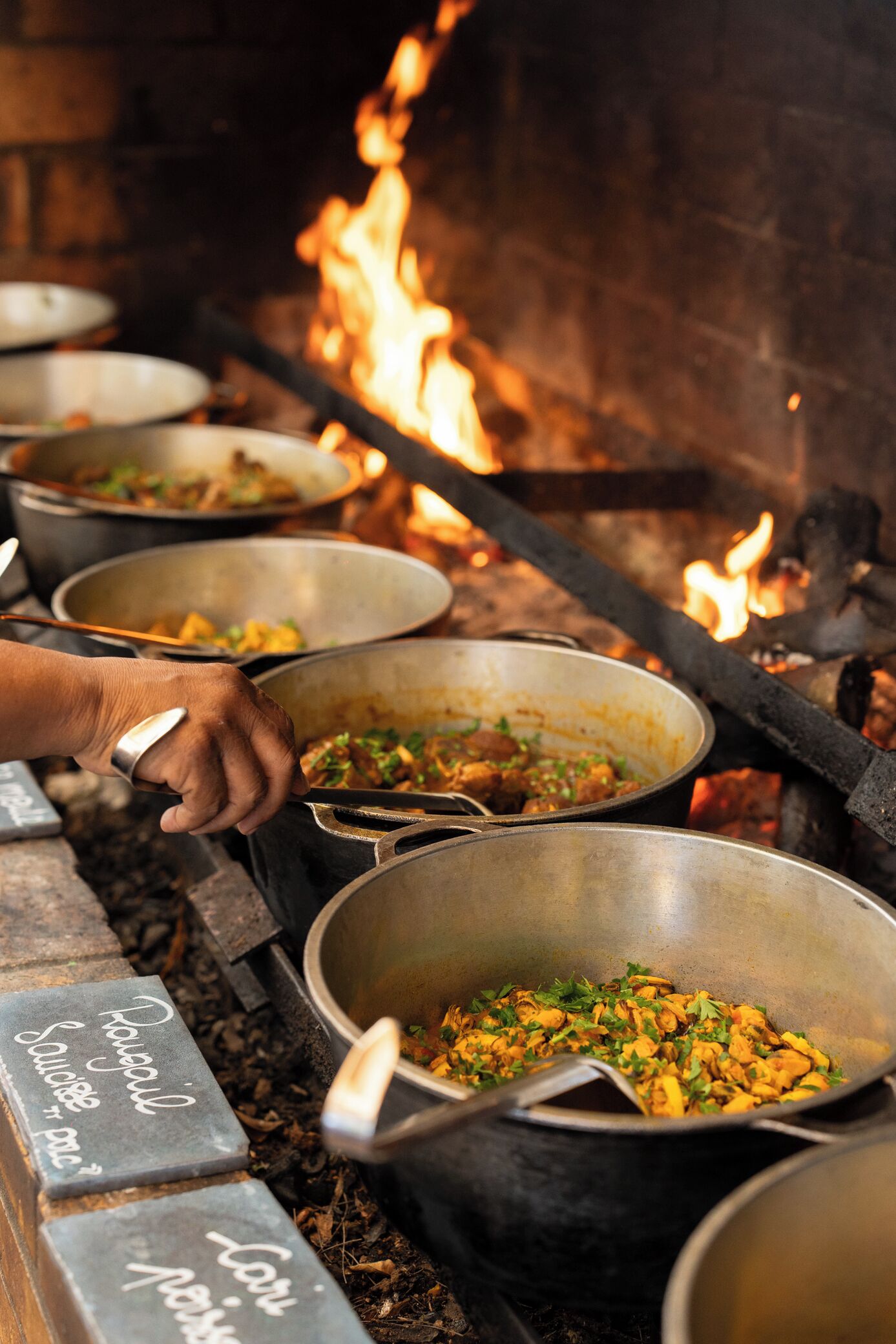 A cooking area with several pots on a stove, surrounded by firewood.
