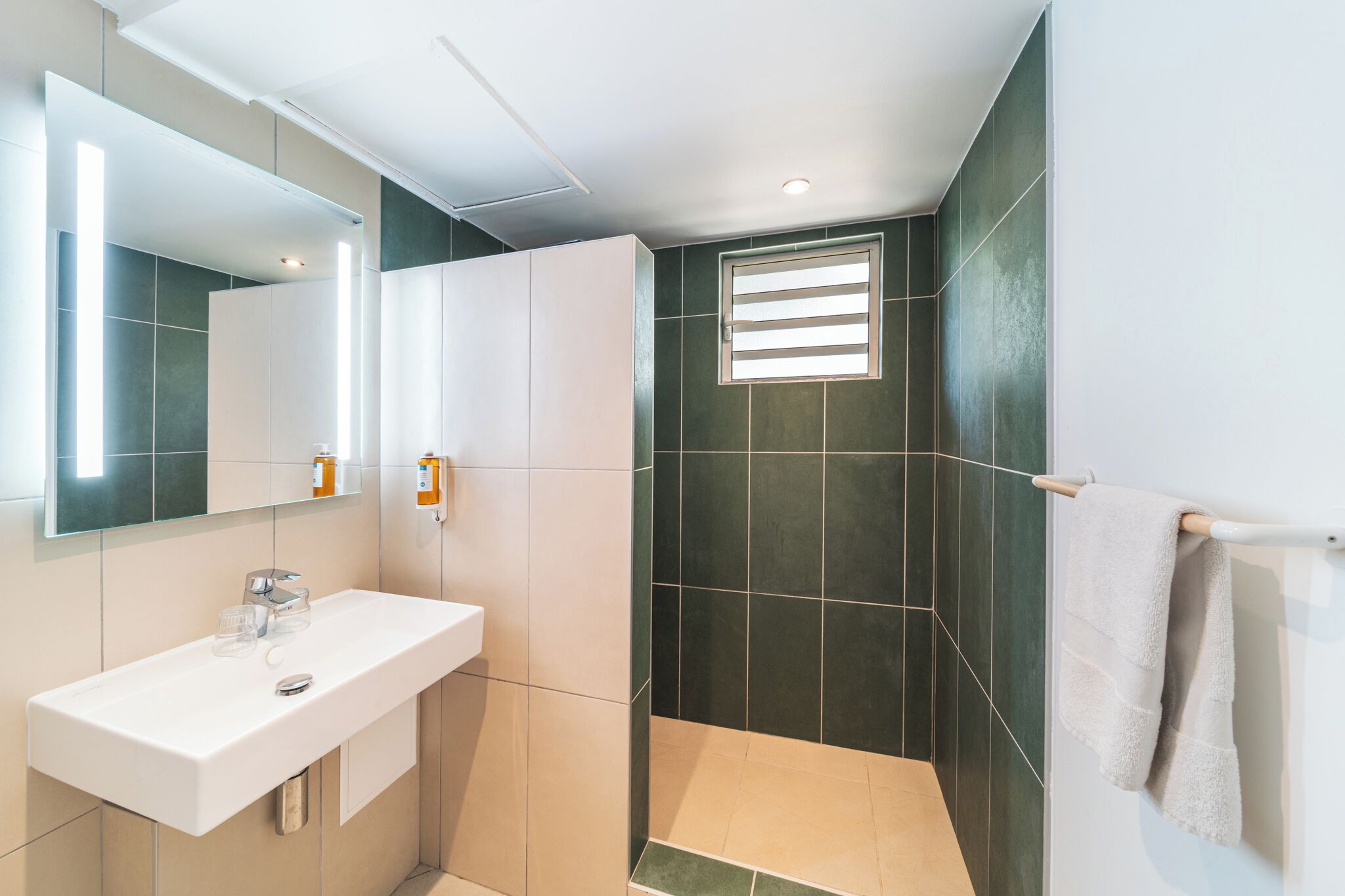 Un baño moderno con un lavamanos blanco, un espejo y una zona de ducha con baldosas oscuras.