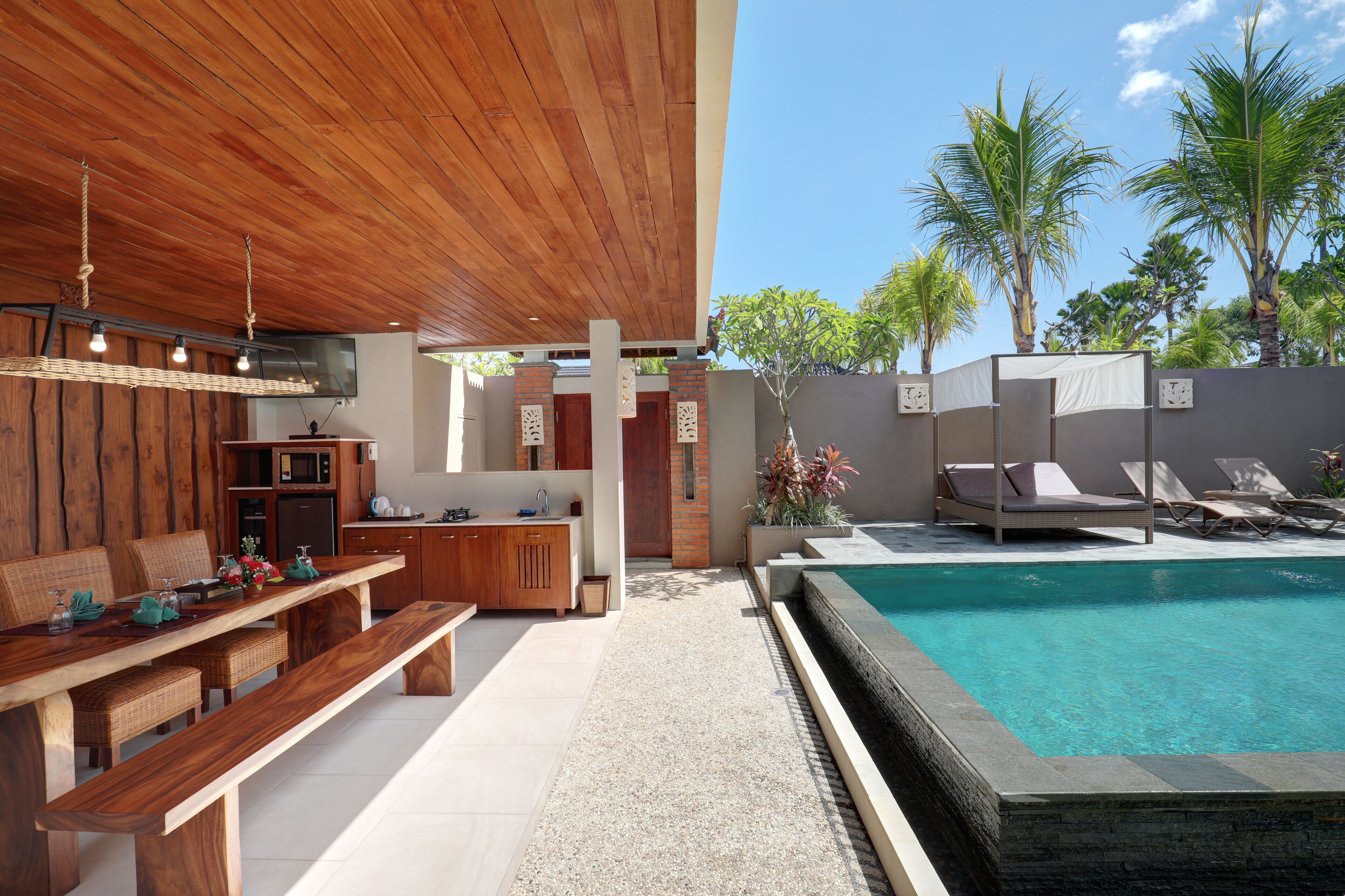 Ein moderner Poolbereich im Freien mit Holzterrasse, Liegestühlen und einer Küchenzeile inklusive Mikrowelle und Spüle.